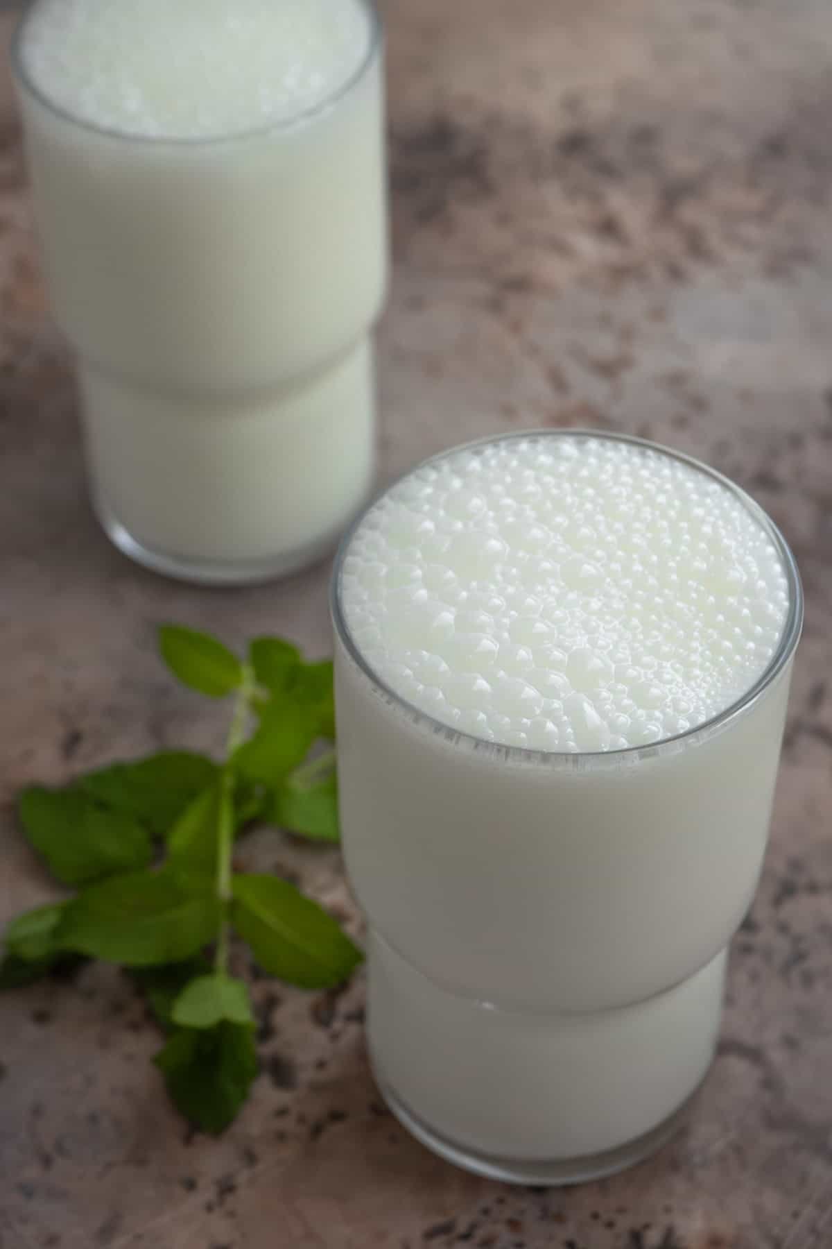 two ayran turkish yogurt drinks in glasses next to a sprig of mint.