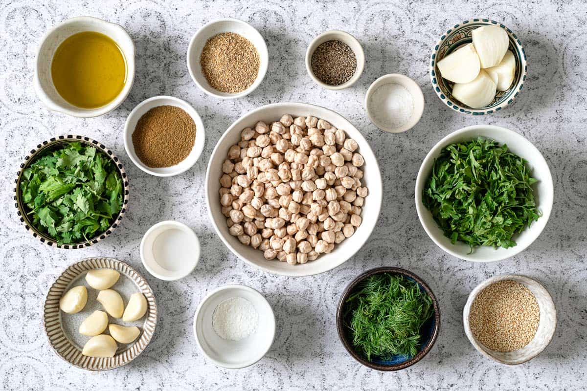 ingredients for baked falafel including dried chickpeas, baking soda, parsley, cilantro, dill, onion, garlic, pepper, salt, cumin, coriander, cayenne, olive oil, baking powder and toasted sesame seeds.