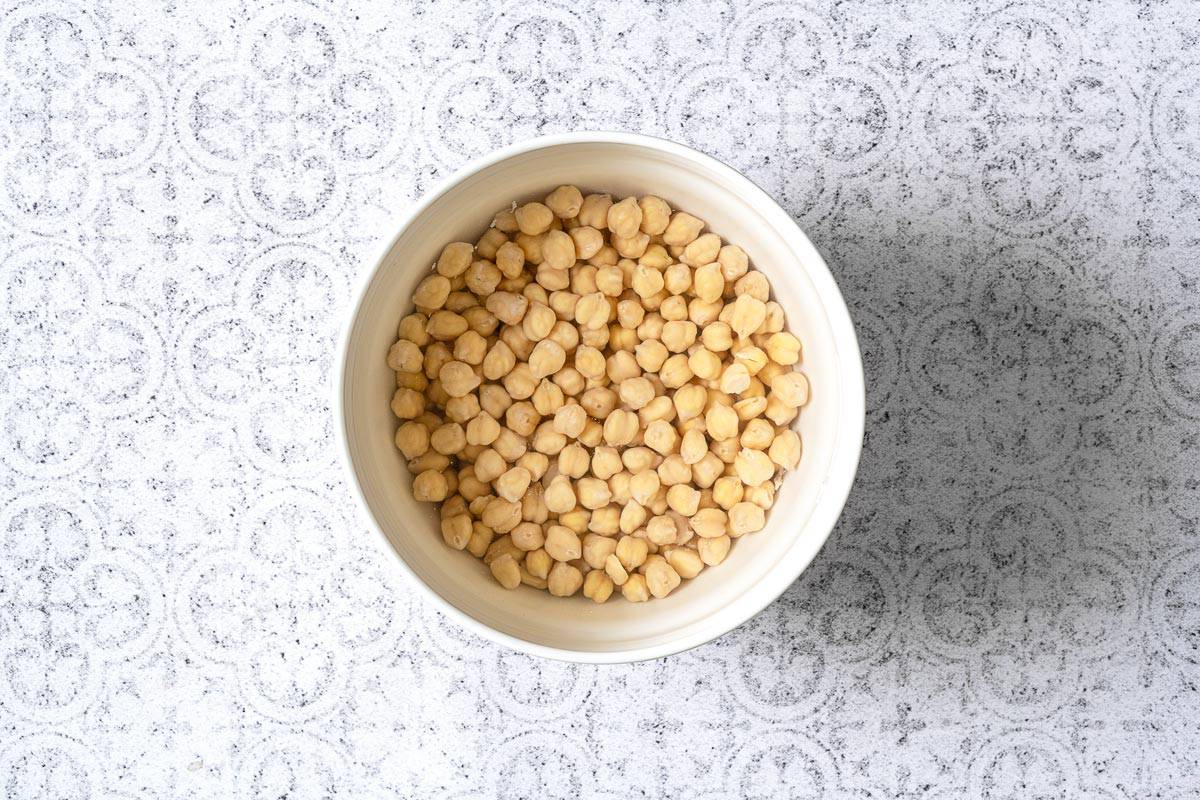 dried chickpeas soaking in a white bowl.