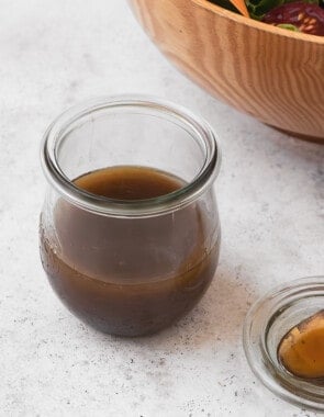 The balsamic vinaigrette recipe in a jar next to a small serving spoon and a bowl of salad.