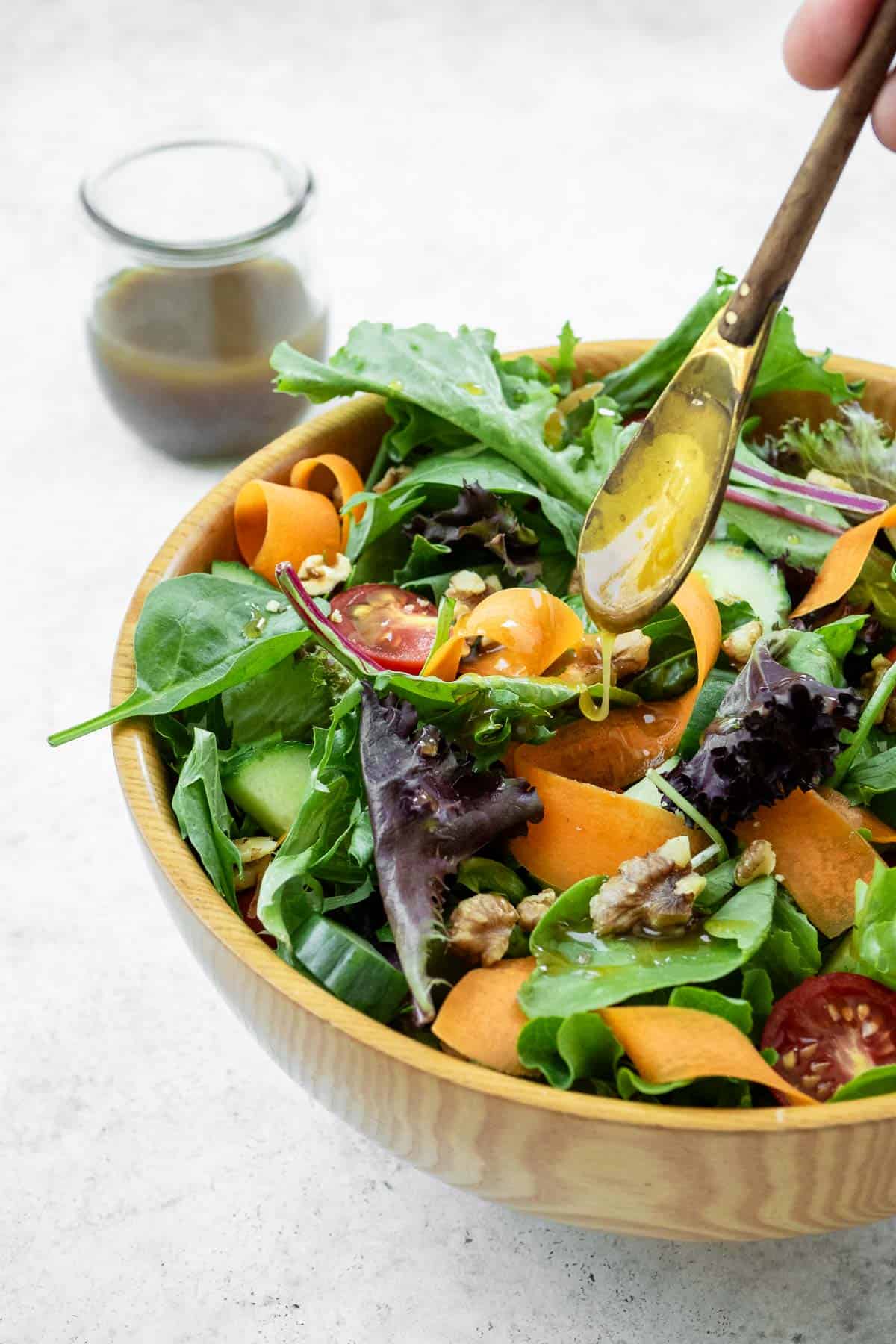 honey balsamic vinaigrette being drizzled from a small serving spoon onto a salad in a bowl.