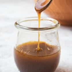 honey balsamic vinaigrette being drizzled from a small serving spoon into a jar of balsamic vinaigrette.
