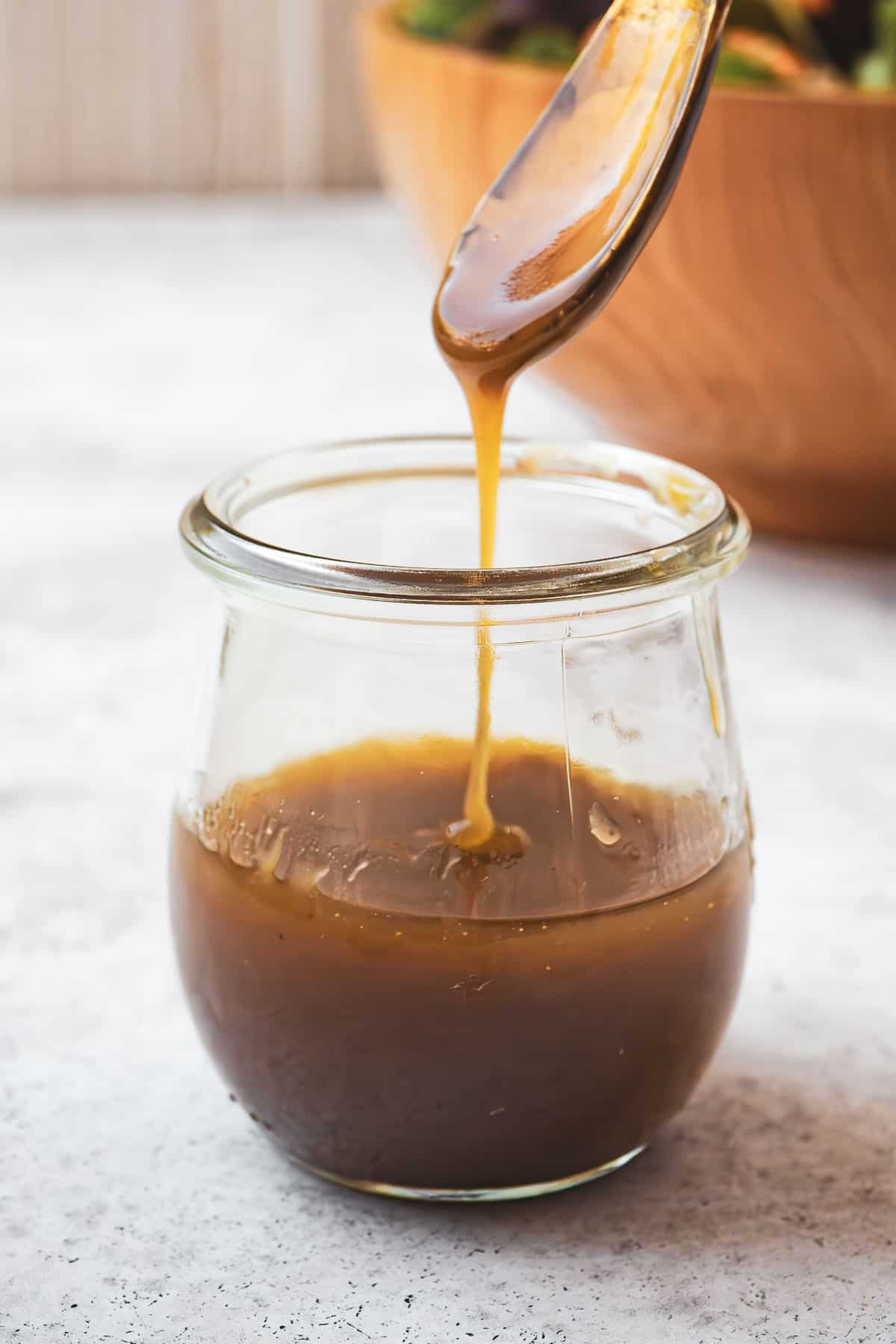 honey balsamic vinaigrette being drizzled from a small serving spoon into a jar of balsamic vinaigrette.