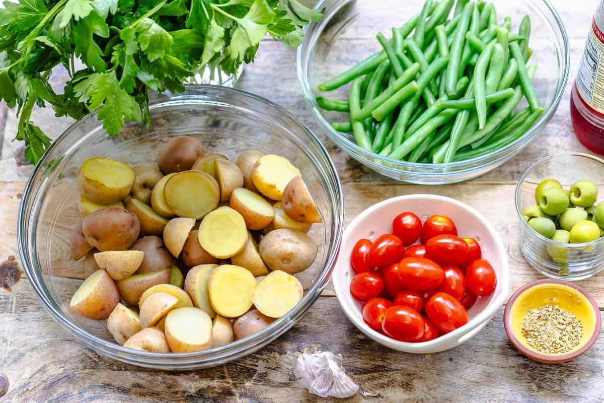 ingredients for italian potato salad including parsley, baby potatoes, green beans, red wine vinegar, garlic, cherry tomatoes, and dried oregano.