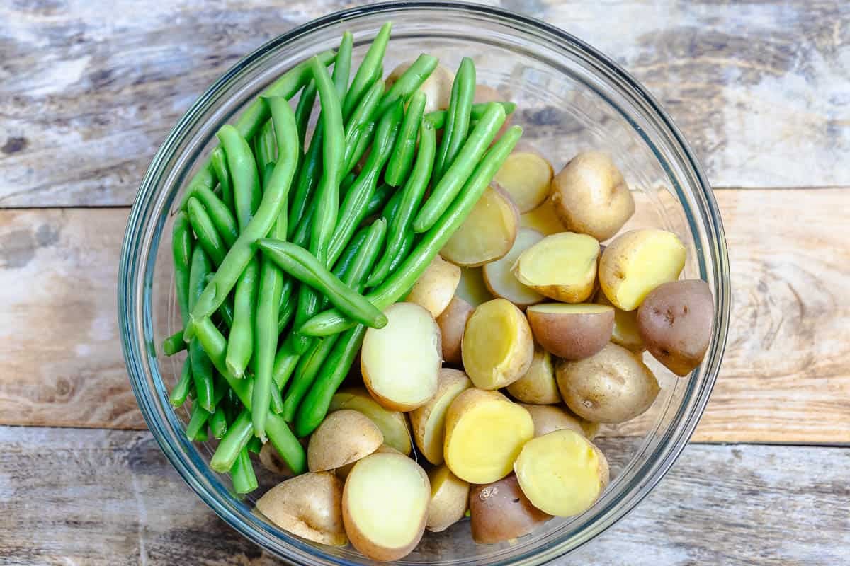 halved baby potatoes and green beans in a glass mixing bowl.
