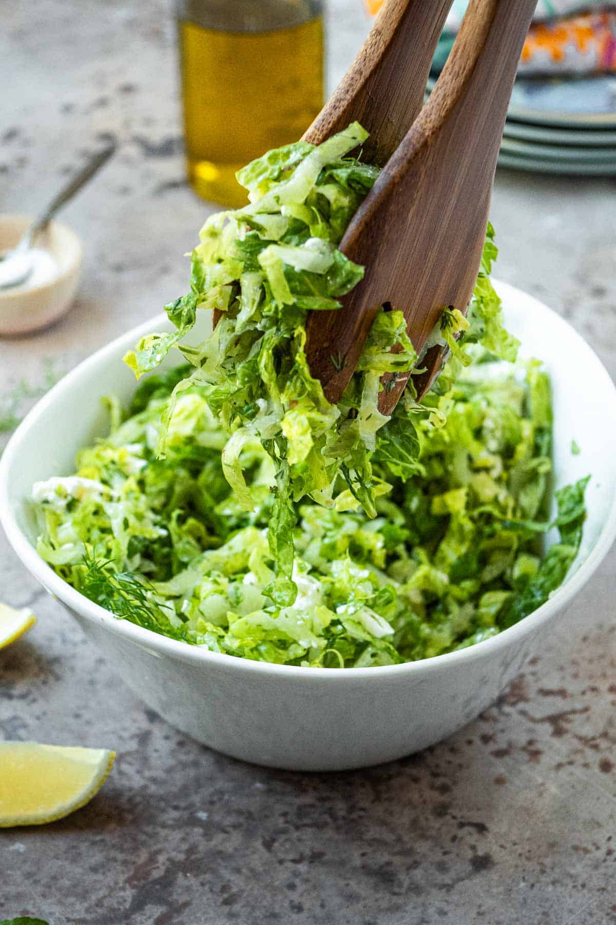 maroulosalata being lifted out of a white serving bowl with wooden utensils.