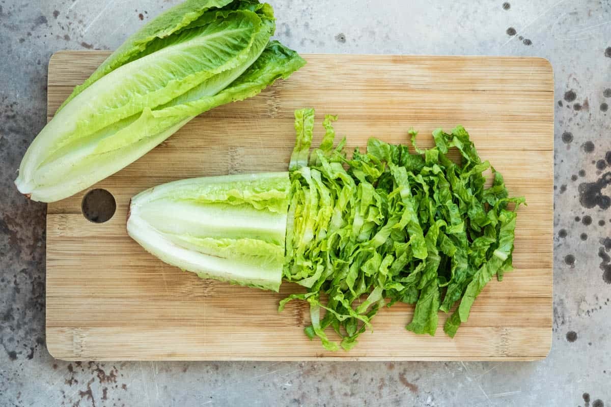 two heads of romaine lettuce on a cutting board, one partially chopped.