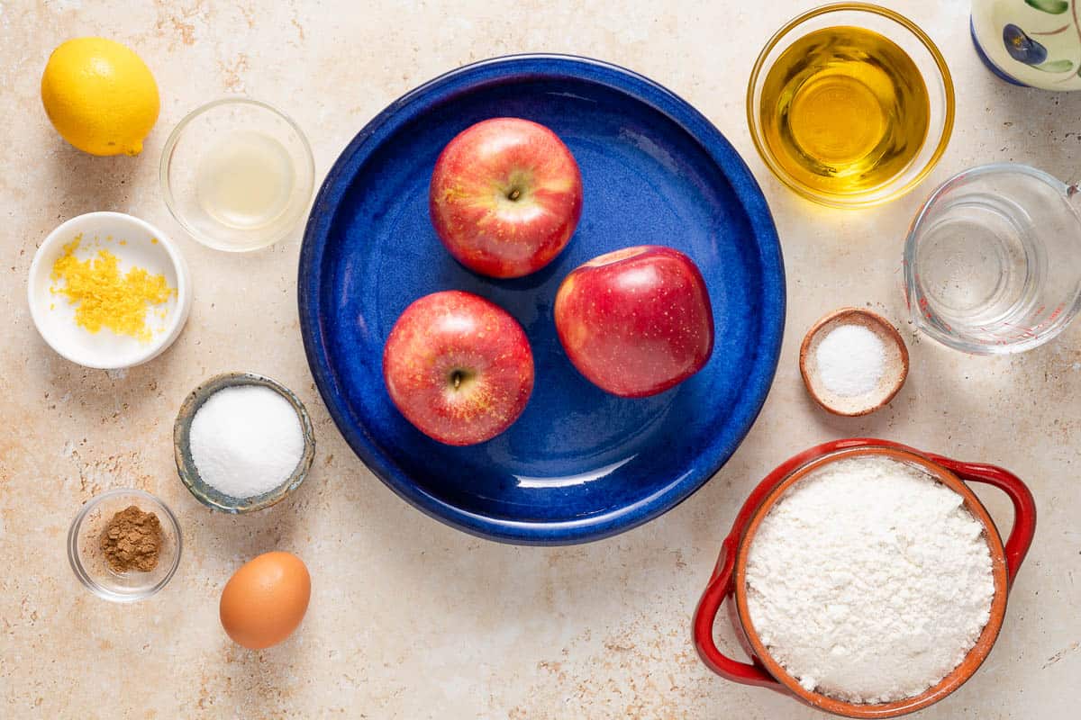 Ingredients for apple emanadas including apples, flour, sugar, salt, olive oil, water, cinnamon, lemon juice, lemon zest, and an egg.