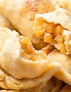 a close up of a baked apple empanada cut in half on a stack of other apple empanadas.