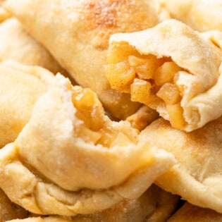 a close up of a baked apple empanada cut in half on a stack of other apple empanadas.