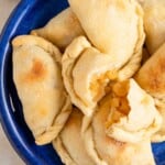 a stack of baked apple empanadas, with one broken in half to show the apple filling on a blue serving plate.