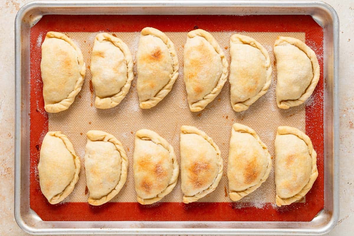 12 baked apple empanadas on a lined baking sheet.
