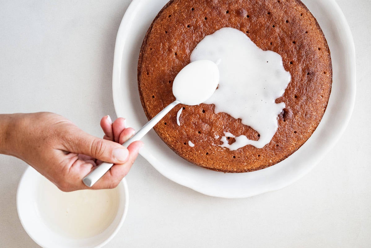 Overhead shot of a person pouring glaze on Persian love cake using a large metal spoon.