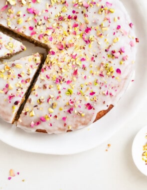 Overhead shot of Persian love cake on a platter with two slices cut out and rose petals and pistachios on the side.