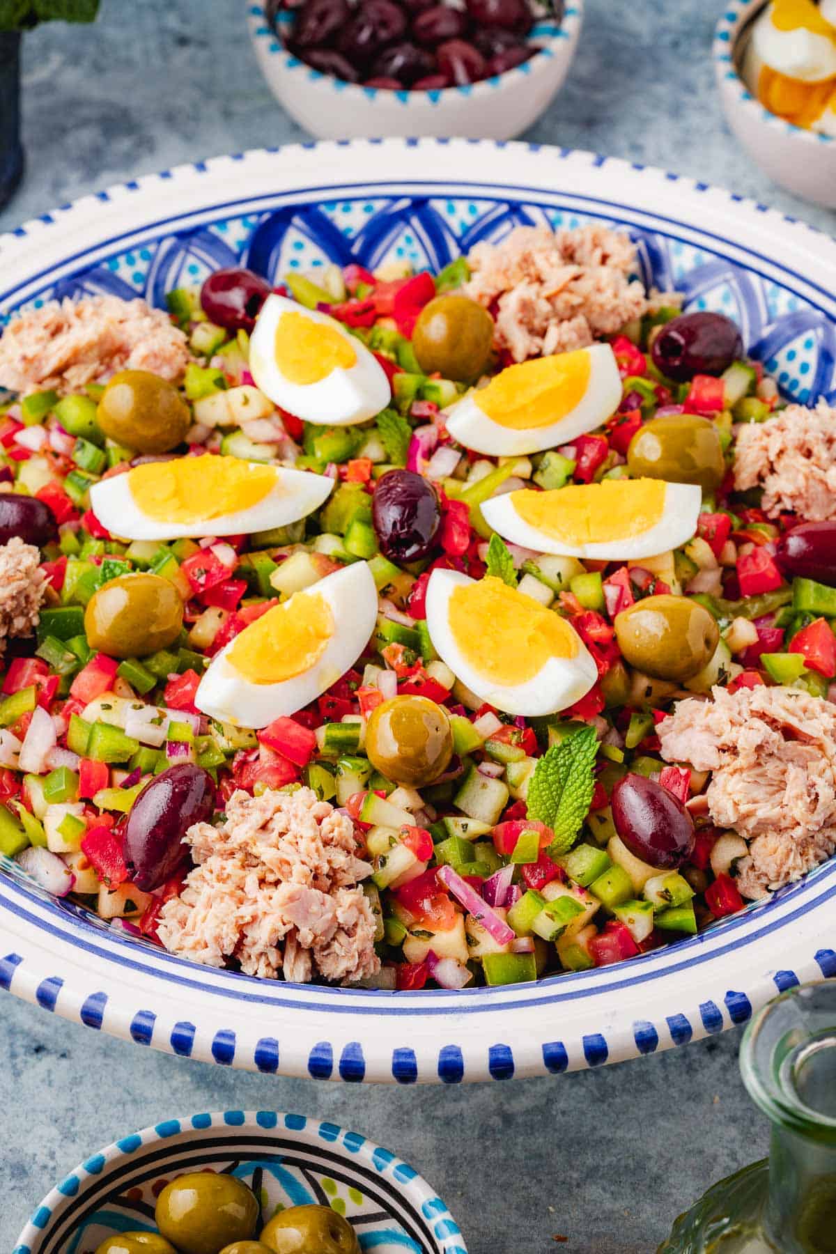 a close up of Slata Tounsiya Tunisian Salad in a serving bowl surrounded by various ingredients.