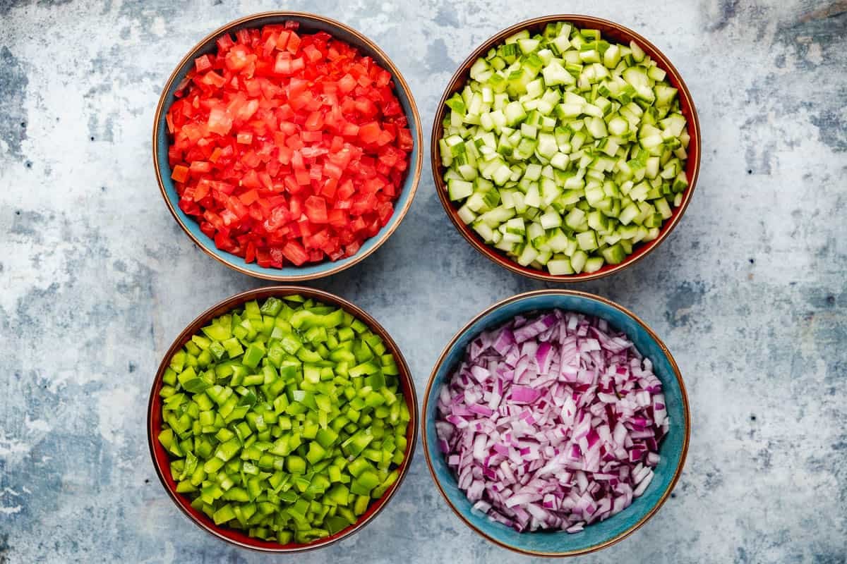 4 bowls containing chopped tomato, chopped cucumber, chopped green pepper and chopped red onion.