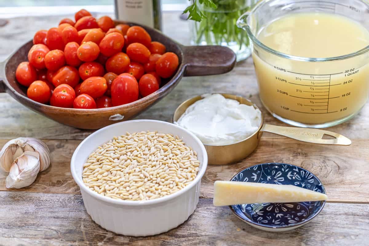 ingredients for creamy orzo including orzo, greek yogurt, chicken broth, cheese, garlic, parsley, olive oil, and cherry tomatoes.