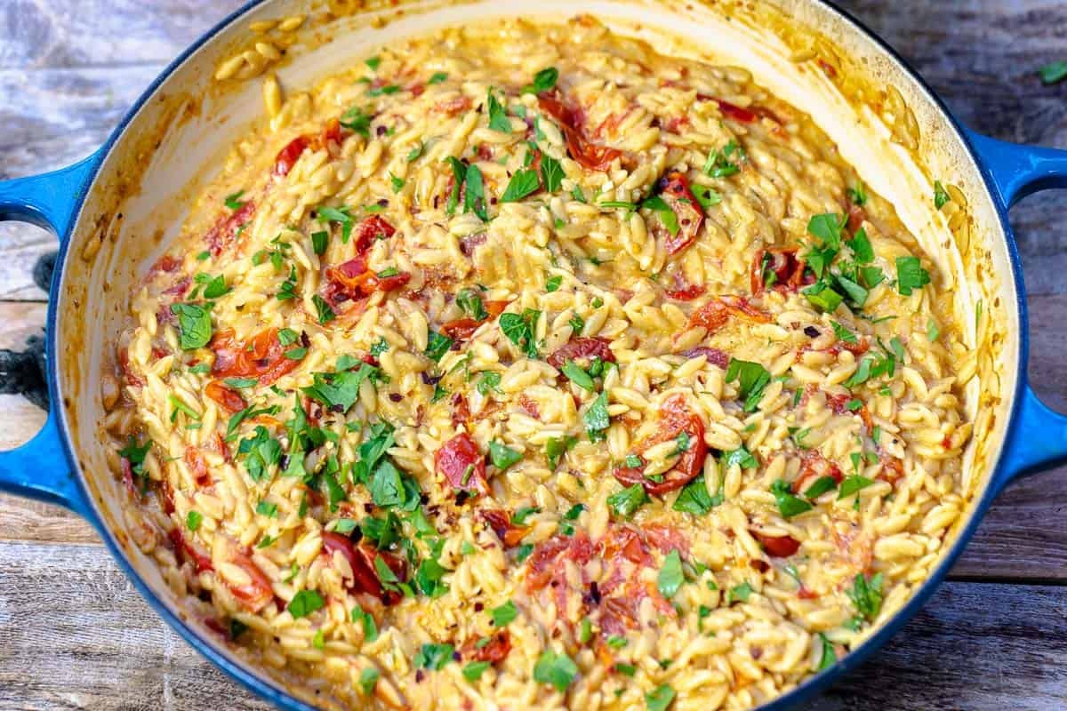 close up photo of creamy orzo in a blue skillet.