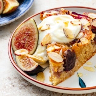 slice of fig cake on a plate with Greek yogurt and sliced almonds on top.