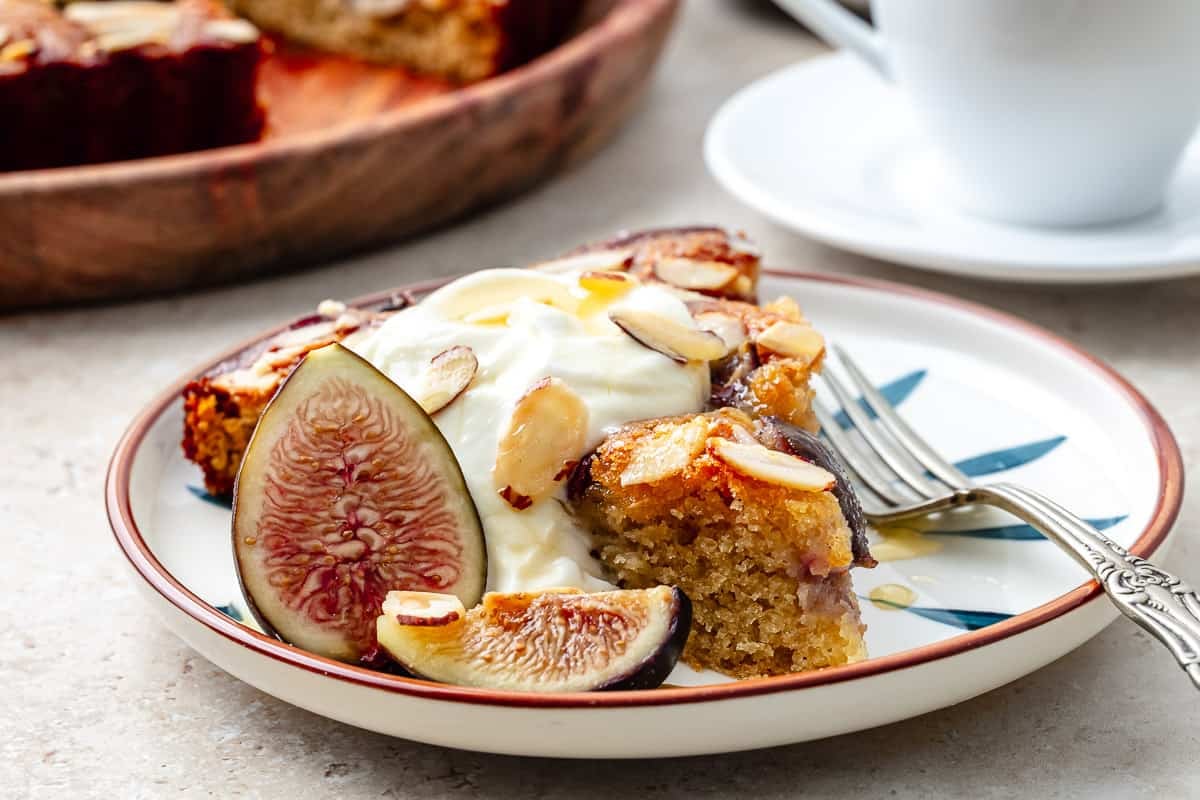 slice of fig cake with Greek yogurt, sliced almonds, and fresh figs on a plate with a fork.