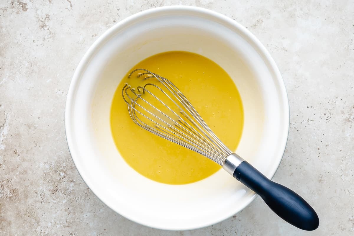 Olive oil, honey, and eggs in a white bowl with a whisk.