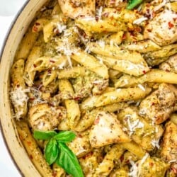 a close up of pesto chicken pasta garnished with basil leaves in a pot.