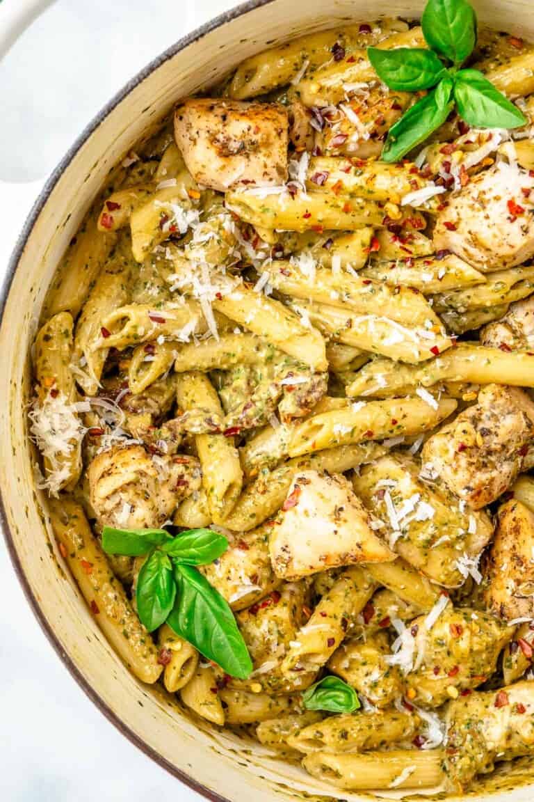 a close up of pesto chicken pasta garnished with basil leaves in a pot.