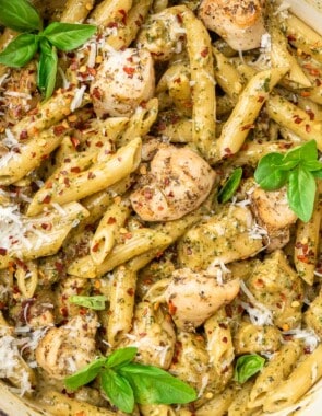 pesto chicken pasta garnished with basil leaves in a pot, next to a small bowl of red pepper flakes.