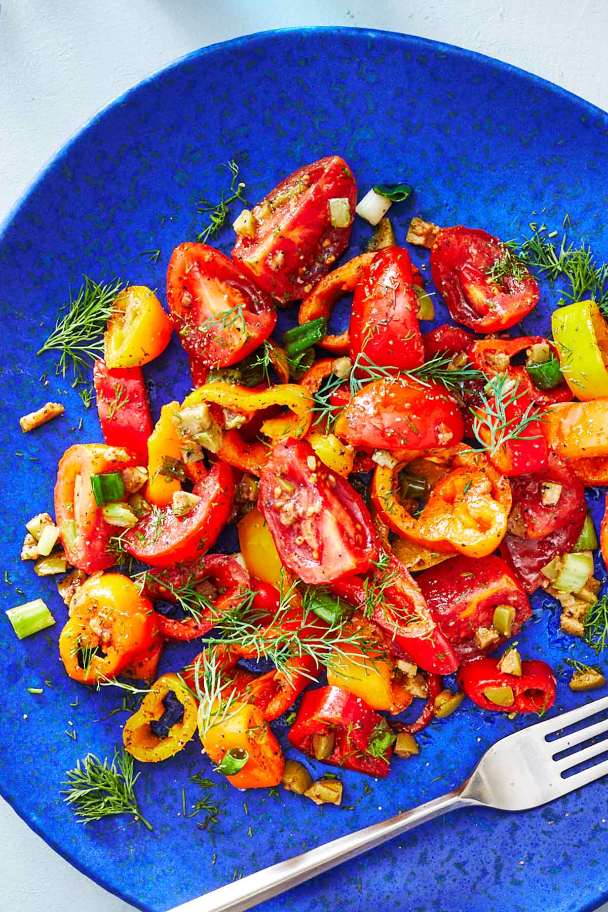 close up of a serving of bell pepper salad on a blue plate with a fork.