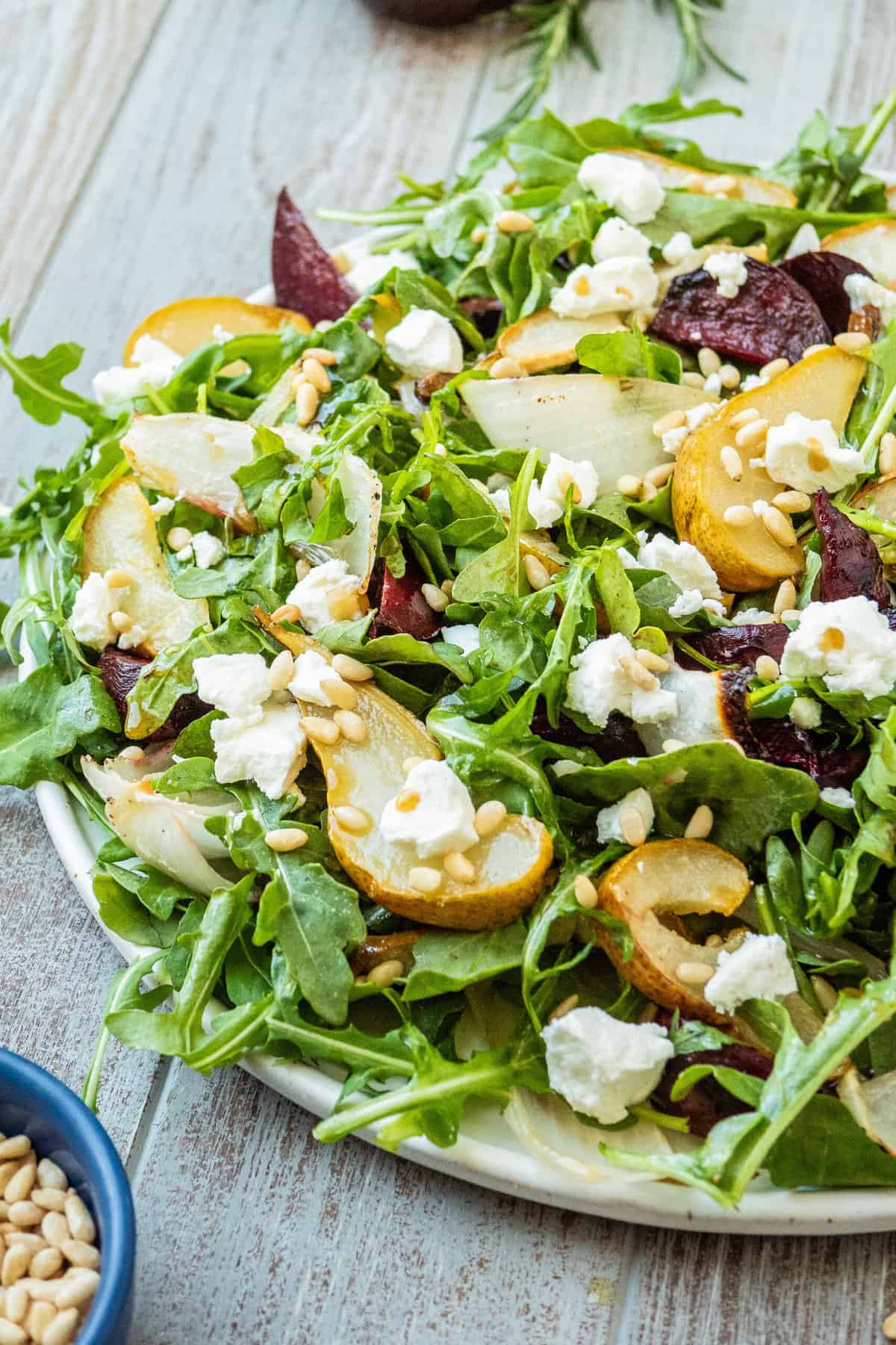 a beet and goat cheese salad on a serving platter next to a small bowl of pine nuts.