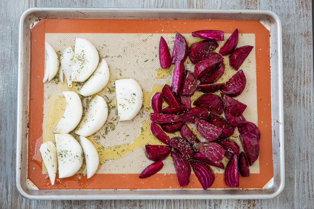 un-roasted onion and beet wedges on a lined baking sheet.