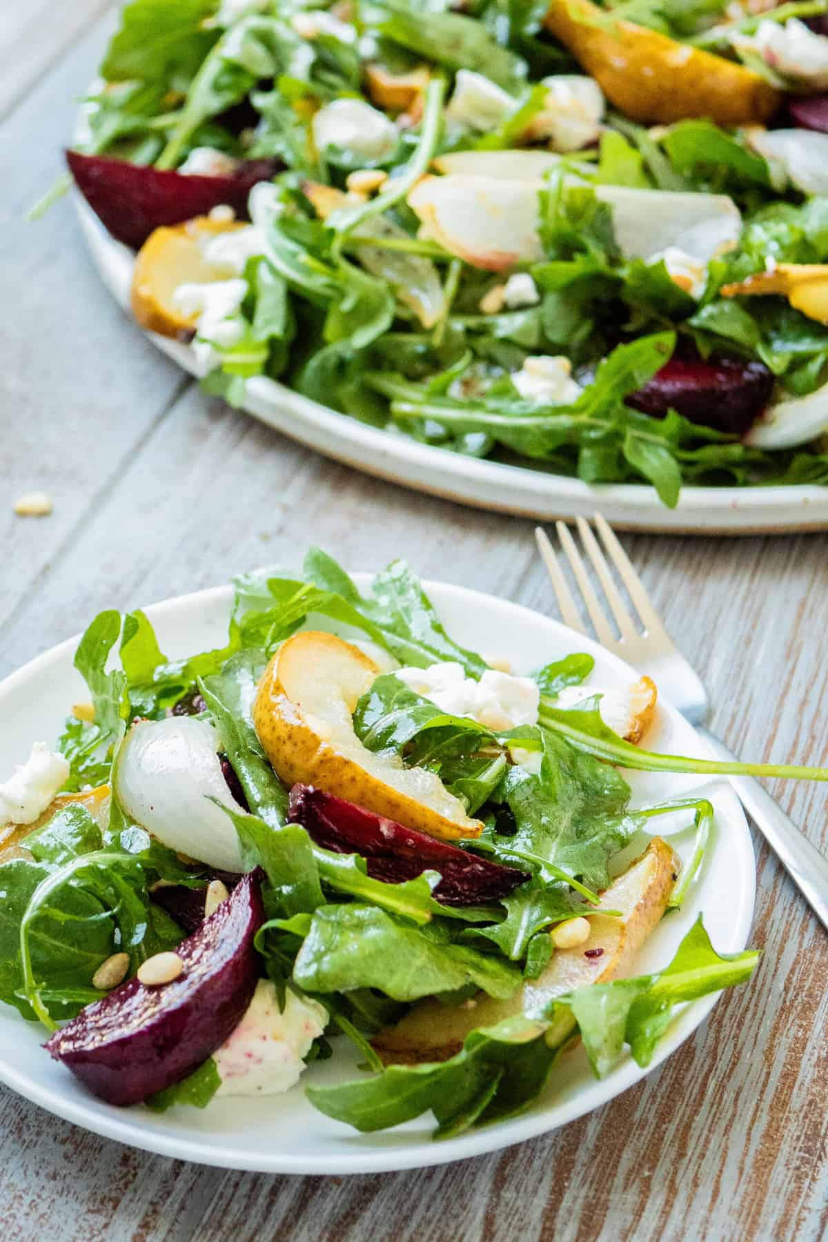 a plate of beet and goat cheese salad and a fork in front of a serving platter with the salad.