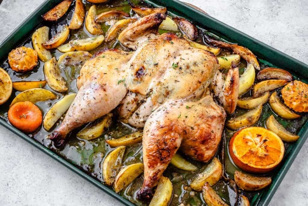 roast spatchcock chicken on a bed of potato wedges and citrus pieces on a sheet pan.