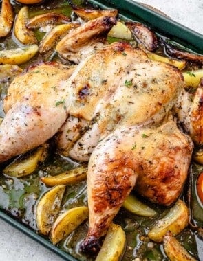 roast spatchcock chicken on a bed of potato wedges and citrus pieces on a sheet pan.
