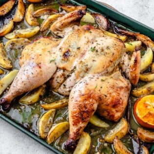 roast spatchcock chicken on a bed of potato wedges and citrus pieces on a sheet pan.