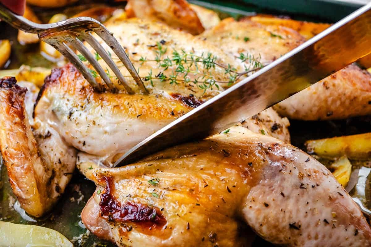 a close up of a knife and fork cutting into the roast spatchcock chicken.