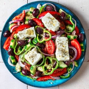 Overhead photo of a Greek salad on a blue serving platter.