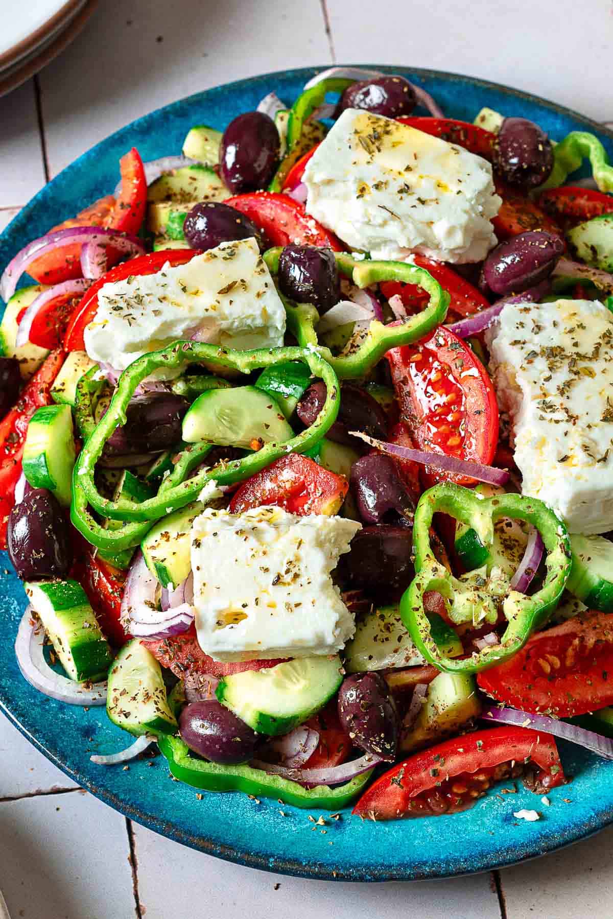 close up of a Greek salad on a blue serving platter.