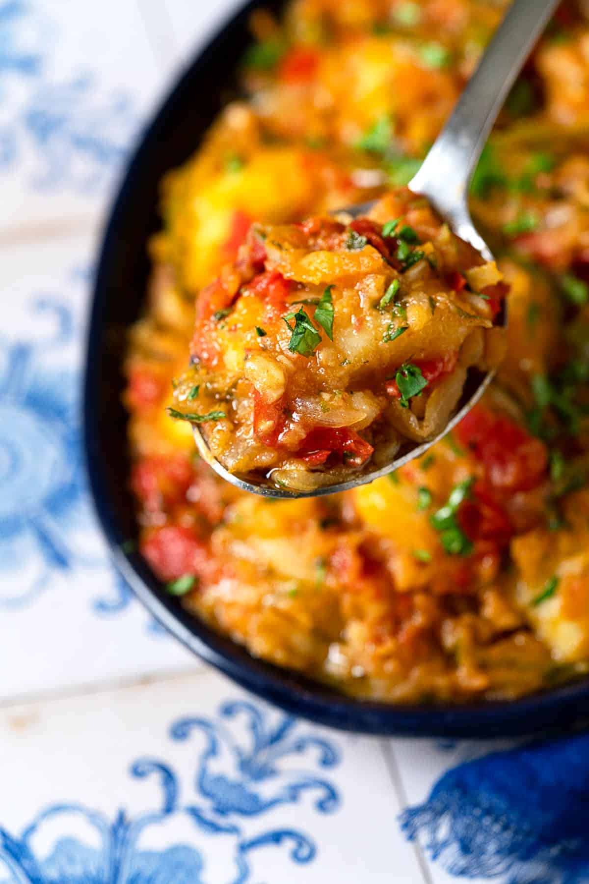 close up of a bite of dopiazeh aloo perisan potato curry being lifted out of a serving bowl with a spoon.