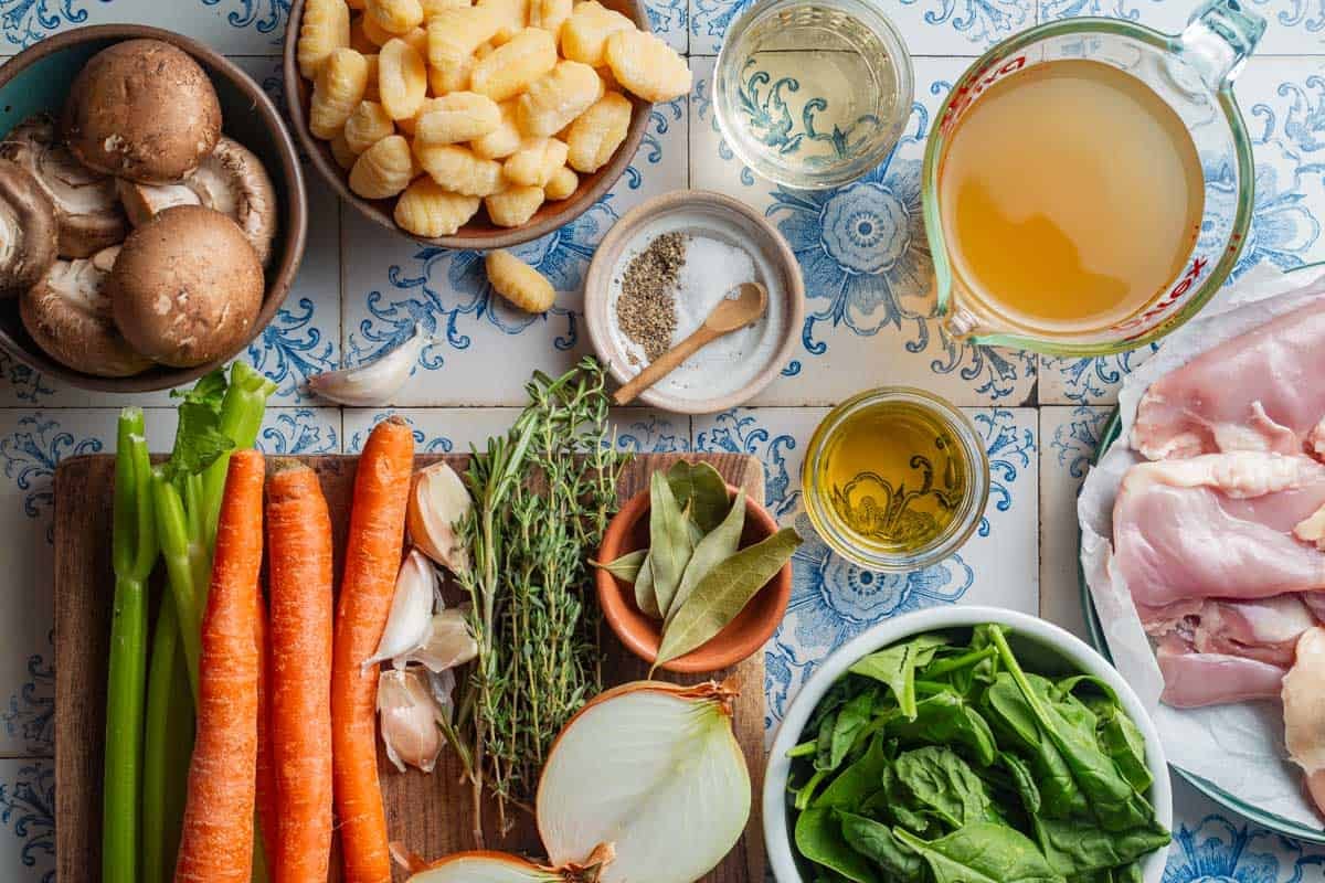 Ingredients for chicken gnocchi soup, including carrot, celery, garlic, thyme, onion, olive oil, chicken stock, spinach, chicken thighs, salt, pepper, gnocchi, and mushrooms.