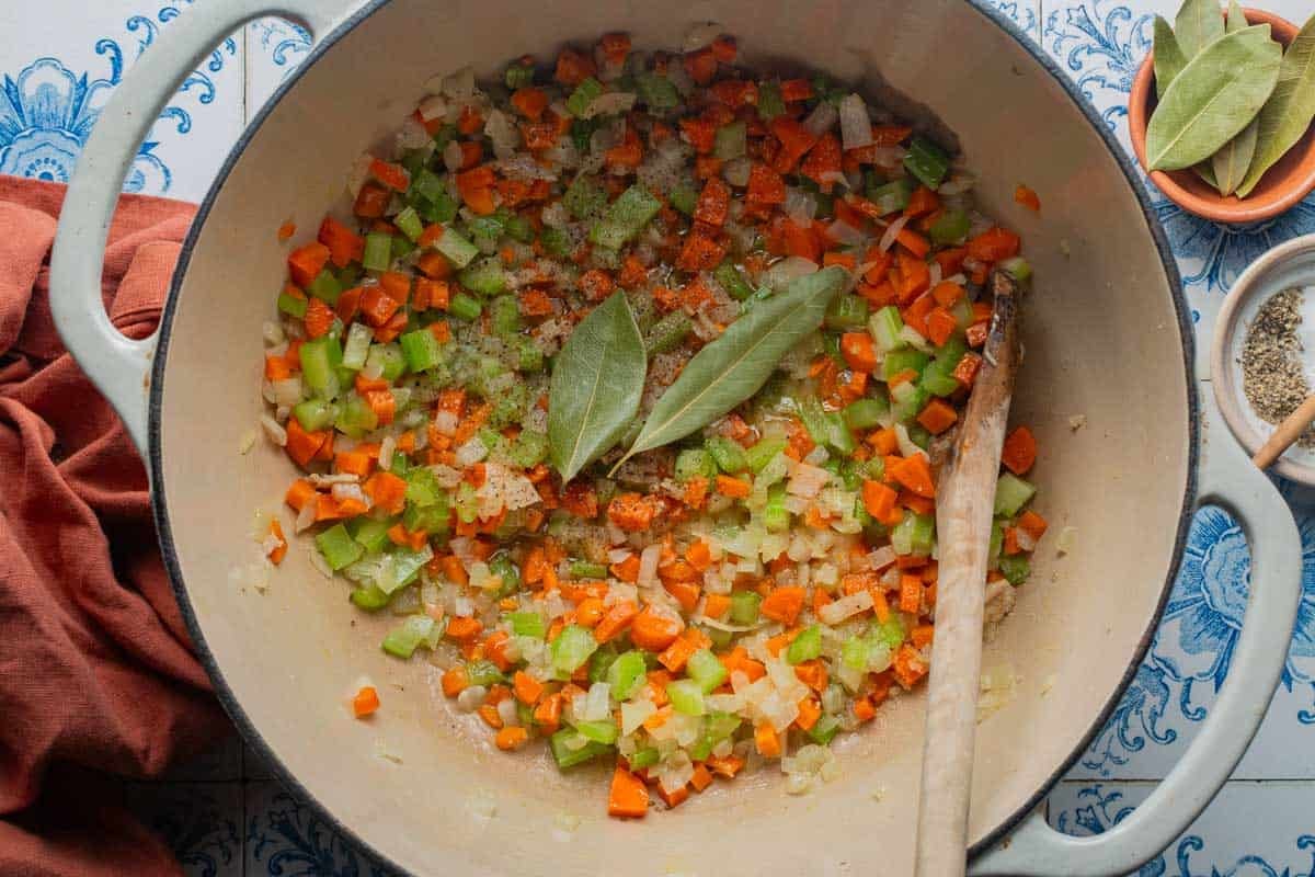 A Dutch oven with carrots, celery, and onion, bay leaves and salt and pepper.