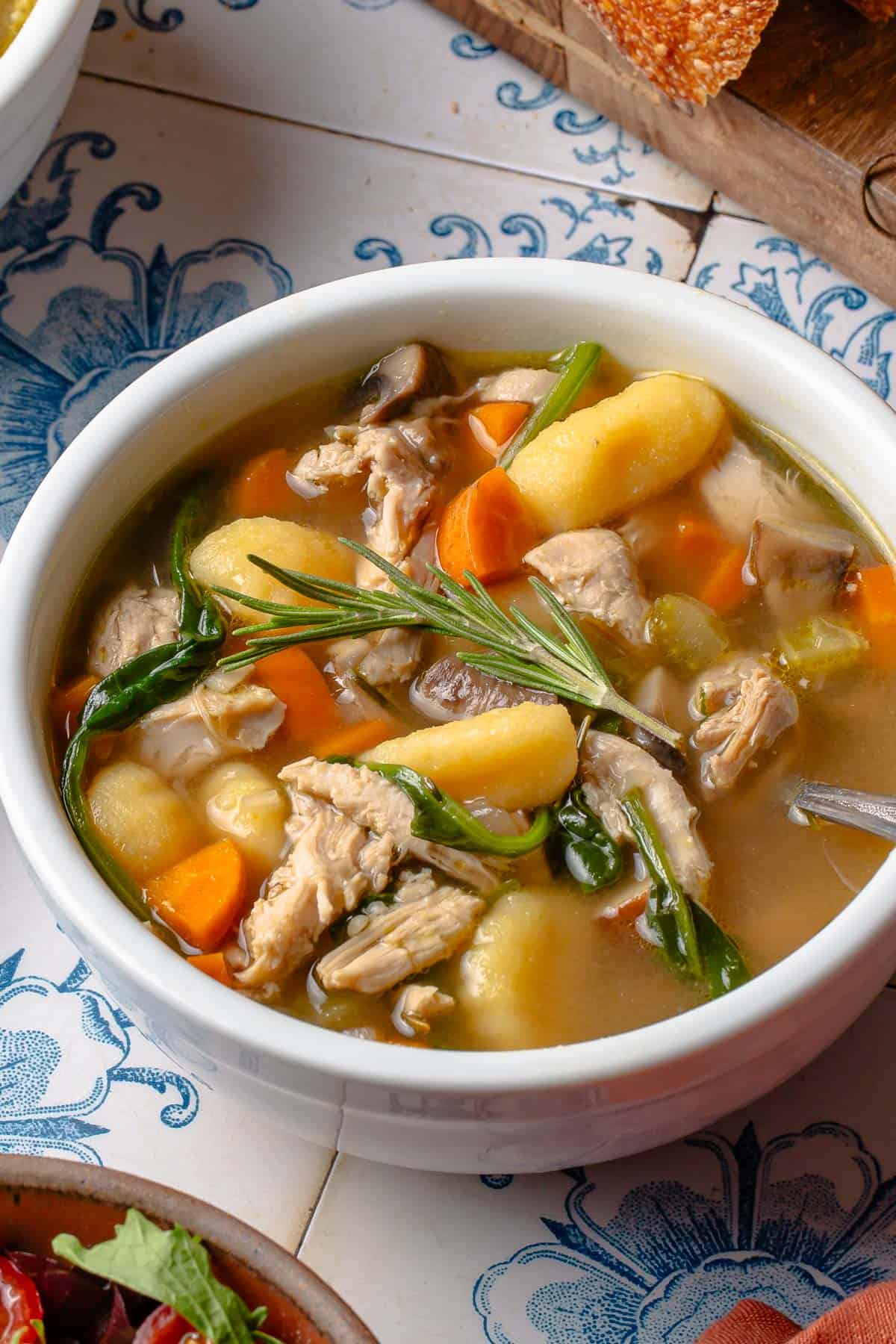 A bowl of chicken gnocchi soup with a sprig of rosemary on top.