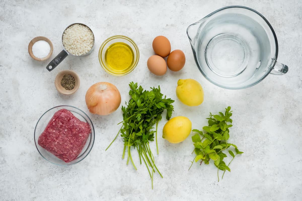 ingredients for Youvarlakia Greek Meatball Soup including ground beef, arborio rice, onion, eggs, parsley, salt, pepper, olive oil, and lemons.