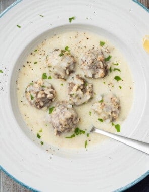 Overhead photo of Youvarlakia Greek Meatball Soup in a bowl surrounded by a small bowl salt and a piece of crusty bread.