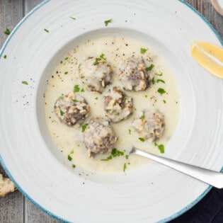 Overhead photo of Youvarlakia Greek Meatball Soup in a bowl surrounded by a small bowl salt and a piece of crusty bread.