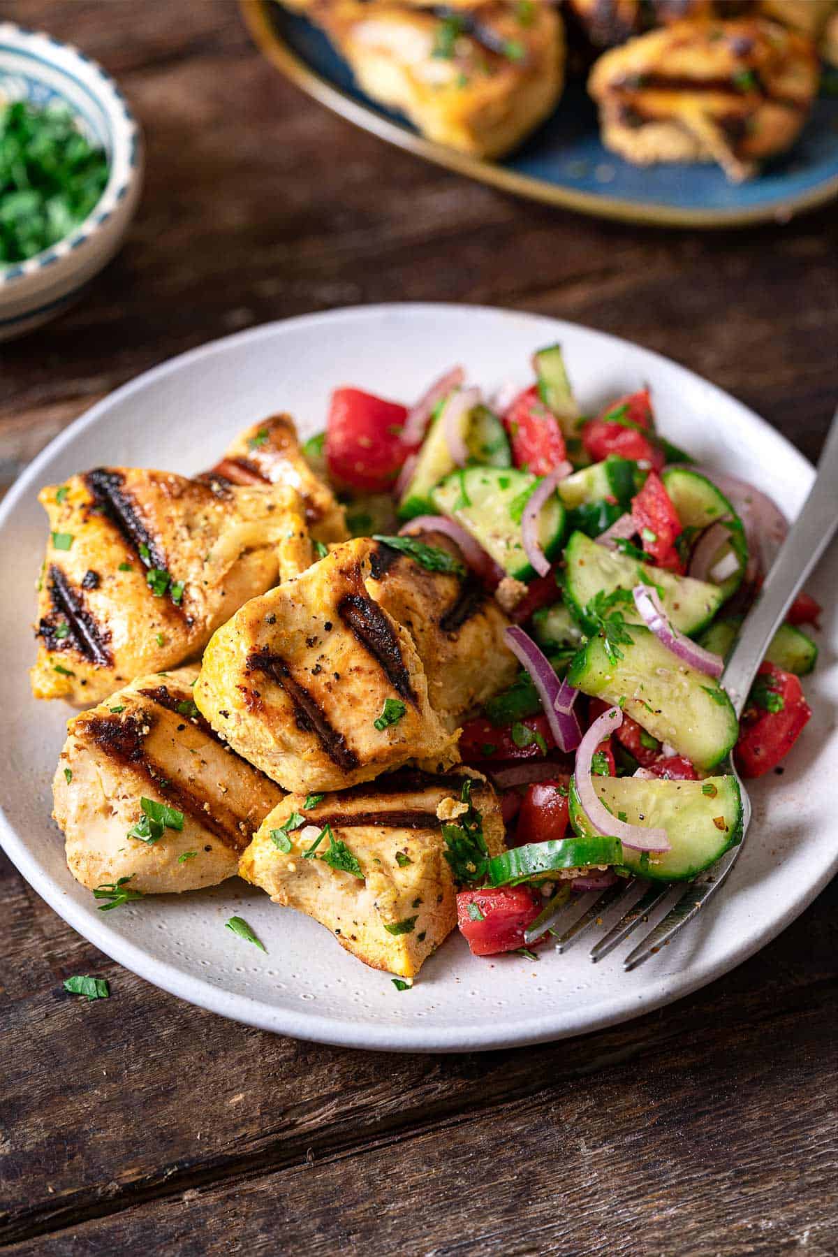 chicken from the joojeh kabobs on a plate with a tomato cucumber salad and a fork. 