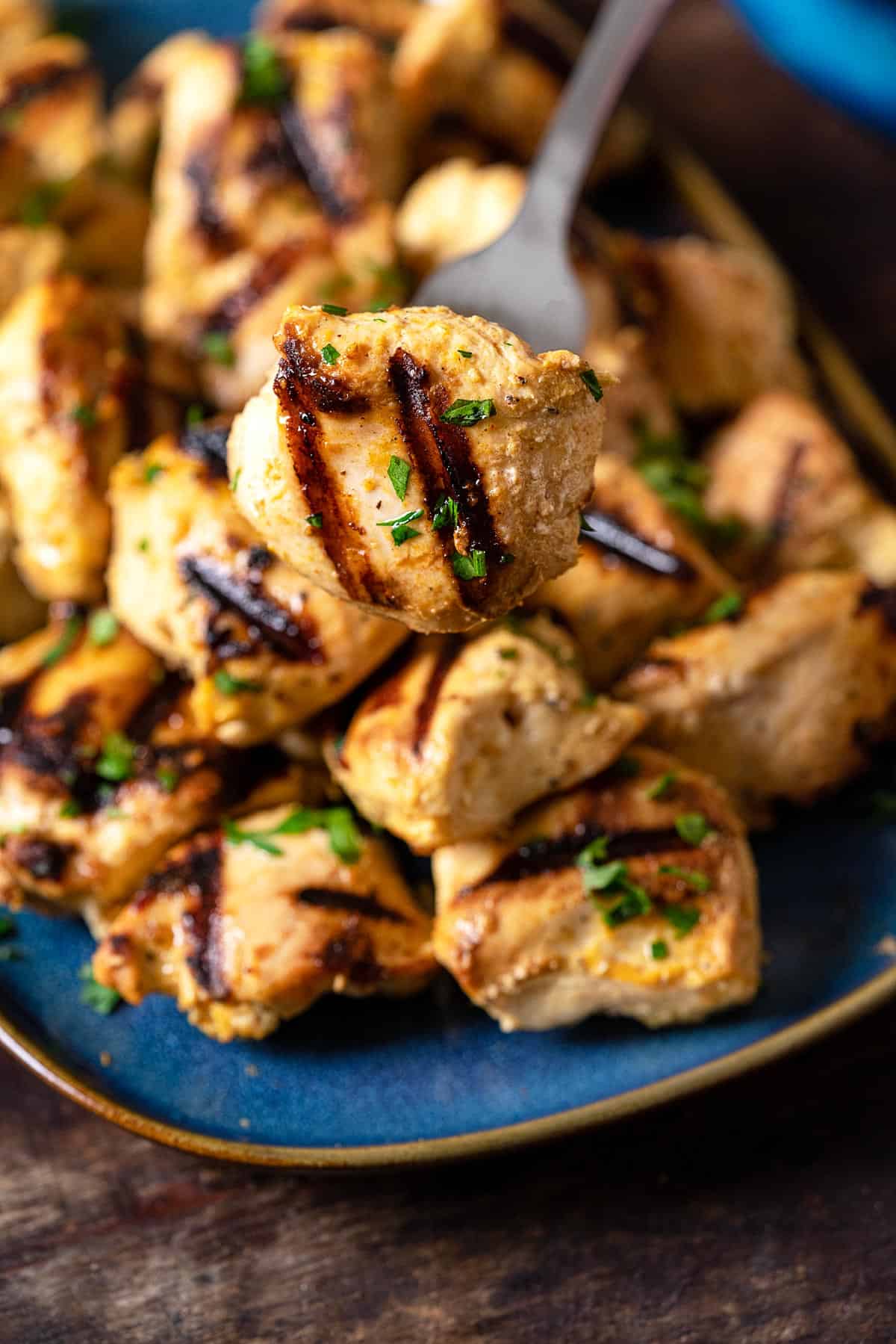 a piece of chicken from a joojeh kabob being picked up from a plate with a fork. 