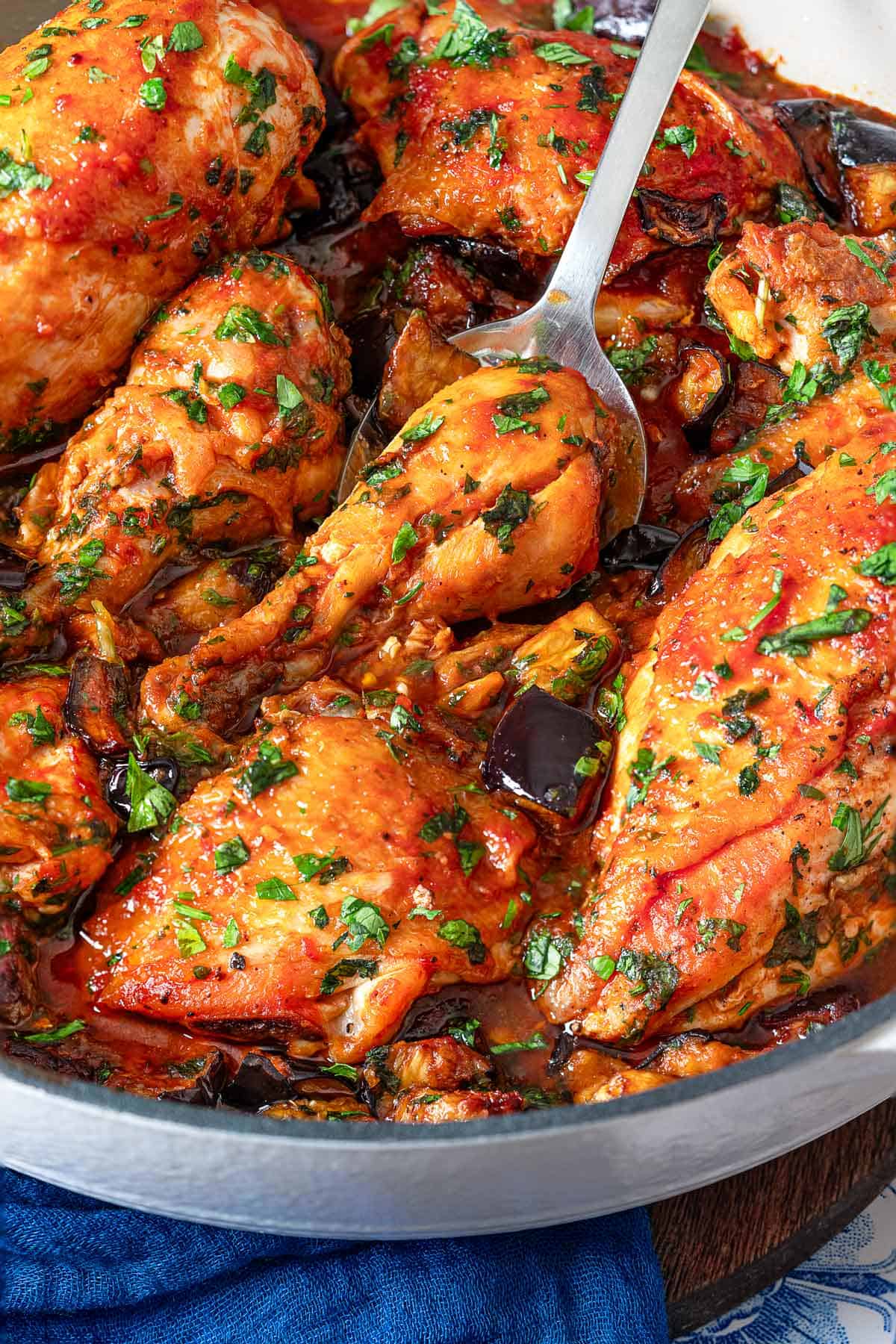 a close up of two cooked Braised Chicken and Eggplant in a skillet with a silver serving spoon.