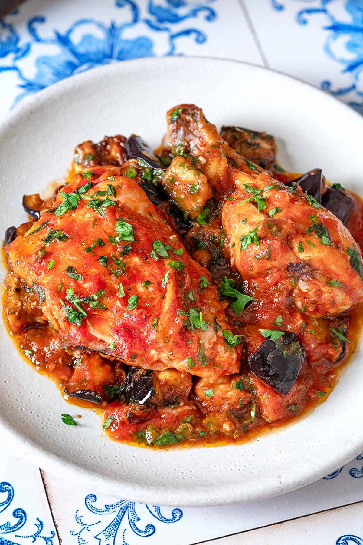 a closeup of two pieces of cooked Braised Chicken and Eggplant on a white plate.