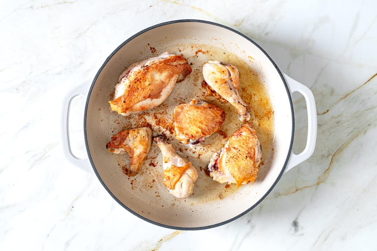 chicken pieces browning in a white skillet.